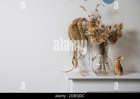 Fleurs séchées et céréales dans un support en verre transparent sur une console blanche dans un intérieur scandinave. Cadre carré. Copier l'espace Banque D'Images