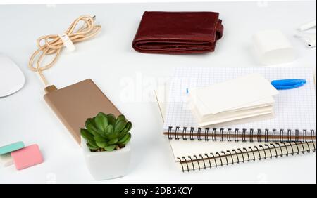 carnets, stylo, pile de cartes de visite, portefeuille en cuir marron et banque d'alimentation avec cordon sur une table blanche, lieu de travail Banque D'Images