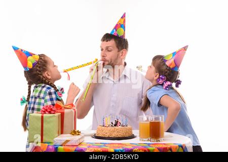 Les enfants et le père soufflent joyeusement les sifflets aux cornes lors d'une fête d'anniversaire Banque D'Images