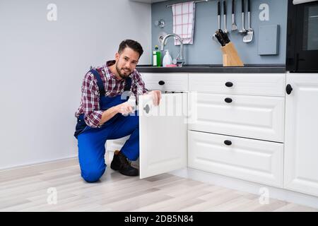 Young Handyman Fixing Sink porte en cuisine Banque D'Images