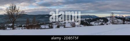 Petit village alpin et hiver montagne enneigée au premier lever du soleil autour, Voronenko, Carpates, Ukraine. Tracer sur un chemin fraîchement trodden à travers g Banque D'Images