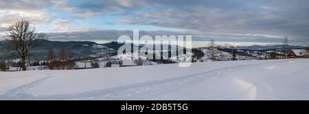 Petit village alpin et hiver montagne enneigée au premier lever du soleil autour, Voronenko, Carpates, Ukraine. Tracer sur un chemin fraîchement trodden à travers g Banque D'Images