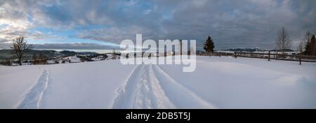 Petit village alpin et hiver montagne enneigée au premier lever du soleil autour, Voronenko, Carpates, Ukraine. Tracer sur un chemin fraîchement trodden à travers g Banque D'Images