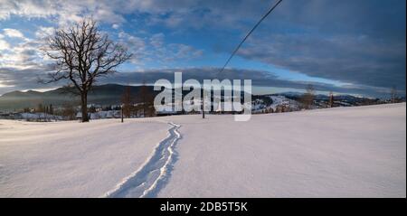 Petit village alpin et hiver montagne enneigée au premier lever du soleil autour, Voronenko, Carpates, Ukraine. Tracer sur un chemin fraîchement trodden à travers g Banque D'Images