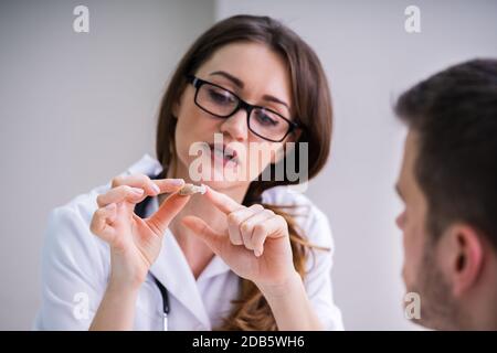 Jeune femme médecin montrant à l'aide auditive Male Patient In Clinic Banque D'Images