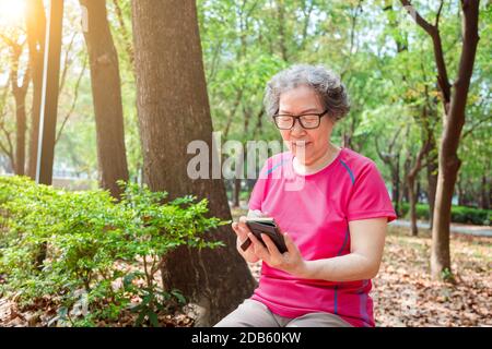 femme asiatique senior dans les verres et la lecture de téléphone mobile Banque D'Images