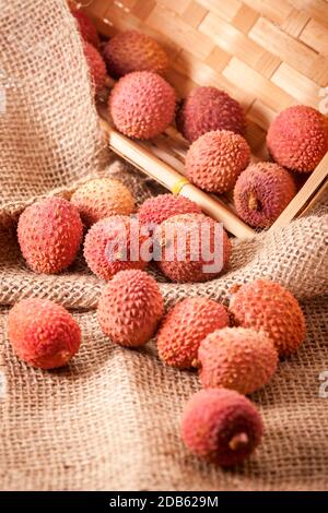 Vue en grand angle d'un panier incliné de fruits (Lichhi) de l'arbre lychee (Litchi chinensis) sur un tissu à grosses sackCloth dans un panier angulaire. Banque D'Images