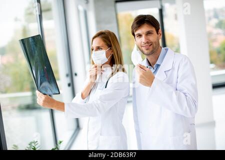 Équipe de médecins examinant la radiographie pendant que le médecin de sexe masculin prend son congé son masque facial de protection dans le bureau médical Banque D'Images
