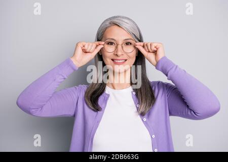 Photo portrait d'une femme aînée souriante et positive qui se touche en gardant le port lunettes en clinique d'ophtalmologie isolées sur fond gris Banque D'Images