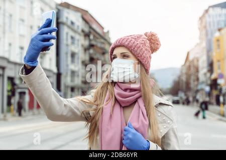 Femme avec masque médical et gants prenant selfie dans la ville de verrouillage ne donnant pas beaucoup sur corona Banque D'Images