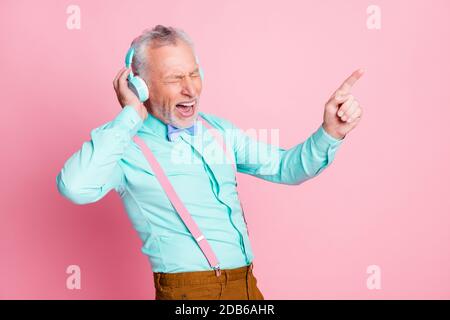 Photo portrait d'un vieil homme qui écoute de la musique avec un casque chant de la chanson préférée pointant avec le doigt isolé sur la couleur rose arrière-plan Banque D'Images