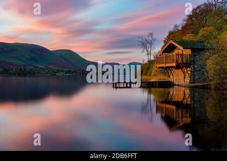 Lever de soleil rose et violet vif avec lumière de l'aube frappant une tour de bateau sur un lac calme avec des réflexions dans le Lake District. Banque D'Images