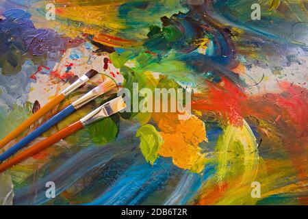 Un groupe de pinceaux artistiques de différentes tailles dans un support de couleur vive devant la palette du peintre. Banque D'Images