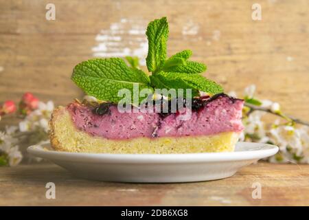 Des tranches de mousse de myrtilles avec des baies décorées de verglas miroir et des feuilles de menthe sur une plaque blanche avec des fleurs blanches sont sur table en bois, à proximité Banque D'Images