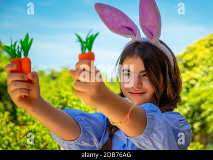 Portrait d'une douce petite fille vêtue d'un lapin, jouant avec des carottes, s'amuser à l'extérieur en journée ensoleillée de printemps, passer Pâques à l'extérieur Banque D'Images