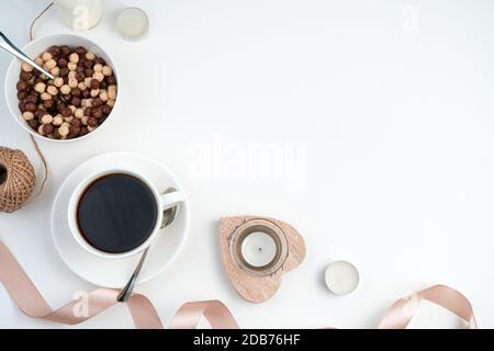 Un fond romantique avec une tasse de café, une assiette de céréales rondes, des coeurs, des bougies et un ruban sur un fond clair. Banque D'Images