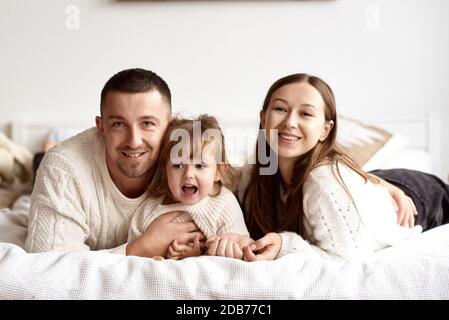Portrait d'une jeune famille heureuse couché au lit souriant et regardant l'appareil photo.