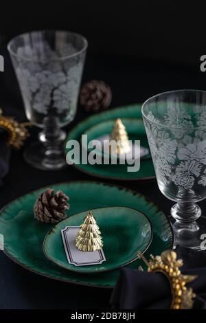 Table de Noël minimaliste liée à une pandémie pour deux - verte assiettes avec décorations de pomme de pin et décorations dorées en forme d'arbre de noël Banque D'Images