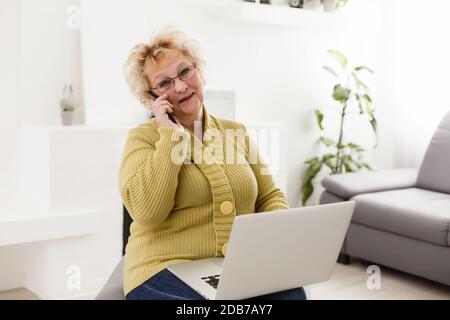 Belle femme âgée assise sur un canapé à la maison, regardant la caméra, fait des appels vidéo, la communication de loin, concept de technologies sans fil modernes Banque D'Images