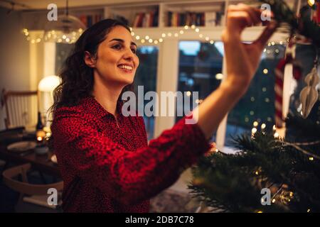 Femme décorant l'arbre de Noël à la maison. Articles décoratifs suspendus par une femme à l'intérieur d'un arbre de Noël. Banque D'Images