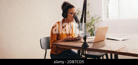 Femme podcaster faisant un podcast à partir de studio à domicile. Femme travaillant à domicile enregistrant un podcast sur un ordinateur portable. Banque D'Images
