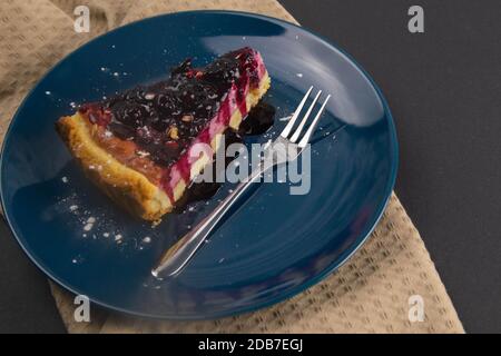 Tranches de gâteau de mousse de myrtille avec glaçage miroir les baies décorées et les feuilles de menthe sur une assiette bleue sont sur table noire, gros plan. Vues de dessus. Banque D'Images