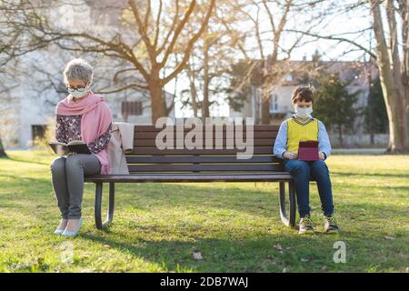 Grand-mère et petit-fils séparés par une distanciation sociale assis sur le banc du parc Banque D'Images