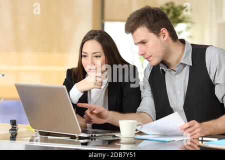 Deux collègues vérifient ensemble le contenu de l'ordinateur portable et comparent les documents au bureau Banque D'Images