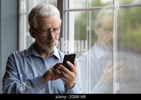 Gros plan homme sérieux et mature portant des lunettes à l'aide d'un téléphone Banque D'Images