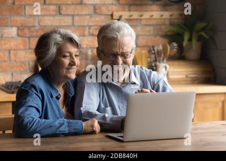 Couple d'âge mûr heureux utilisant un ordinateur portable ensemble, en faisant des achats ou en discutant en ligne Banque D'Images