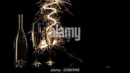 Des verres et une bouteille de champagne dans les lumières du Bengale. Arrière-plan noir. Concept de célébration et nouvel an. Banque D'Images