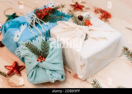 Concept de noël sans gaspillage. Boîtes-cadeaux enveloppées dans un tissu avec branche d'épinette et baies sur fond de bois. Mise à plat. Écologique durable Banque D'Images