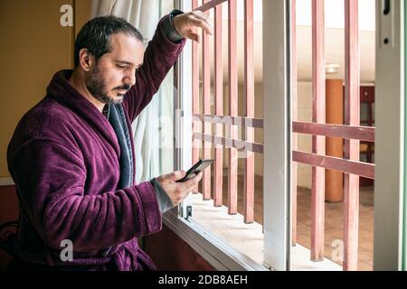 homme regardant dans la fenêtre et utilisant le smartphone Banque D'Images