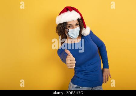 Femme avec chapeau de Noël est optimiste au sujet de la défaite de covid 19 coronavirus. Fond jaune. Banque D'Images