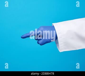 homme medic en manteau blanc, portant des gants stériles bleus, montrant un geste de la main indiquant le sujet, fond bleu Banque D'Images