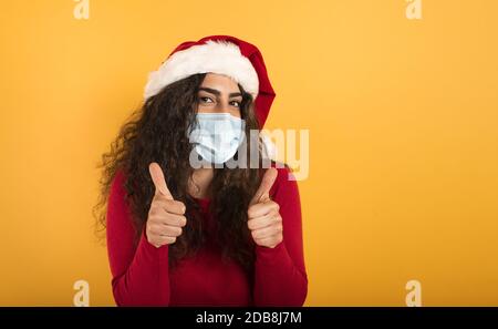 Femme avec chapeau de Noël est optimiste au sujet de la défaite de covid 19 coronavirus. Fond jaune. Banque D'Images