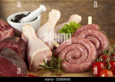 Assortiment de viandes fraîches brutes pour griller avec des pattes de poulet, des steaks de boeuf et des serpentins de saucisse sur un fond en bois avec des herbes et des épices en gros plan Banque D'Images