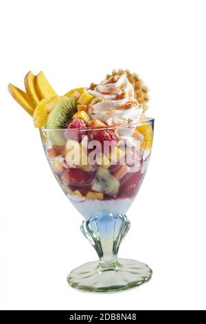 Dessert de salade de fruits tropicaux avec fruits frais et crème glacée servis dans un plat en verre sur pied, vue latérale isolée sur le blanc Banque D'Images