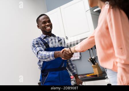 Réparateur de jeunes hommes en serrant la main d'Happy Woman in Kitchen Banque D'Images