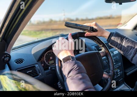 jeune homme avec arme à feu en main dans la voiture de tourisme sur le siège conducteur. Banque D'Images