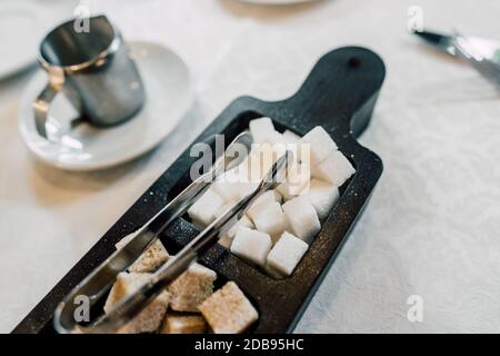 Bol avec morceaux de cubes de sucre blanc et brun et pinces à sucre. Banque D'Images