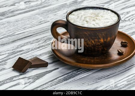 Café mousse fort dans une tasse en céramique sur une table en bois clair. Il y a deux grains de café sur une soucoupe et deux morceaux de chocolat noir sur le Banque D'Images