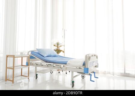 Nettoyer et nettoyer l'hôpital vide près de la fenêtre ensoleillée, linge de lit bleu avec rideau blanc dans la salle d'hôpital pour l'arrière-plan Banque D'Images