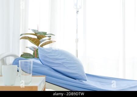 Nettoyer et nettoyer l'hôpital vide près de la fenêtre ensoleillée, linge de lit bleu avec rideau blanc dans la salle d'hôpital pour l'arrière-plan Banque D'Images