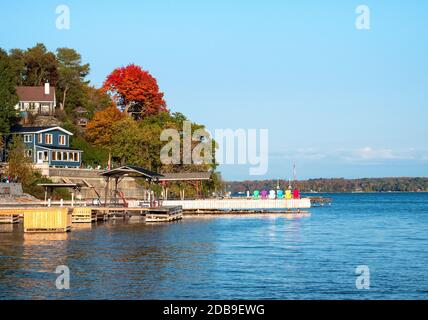 Paisible lac où une jetée blanche avec chaises hautes en couleur s'étend vers l'extérieur. Paysage de chalet sur le fleuve Saint-Laurent de l'Ontario, Canada. Banque D'Images