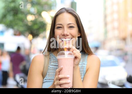 Vue avant portrait d'une heureuse fille regardant appareil photo boire milkshake dans la rue Banque D'Images