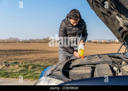 l'homme verse dans le liquide jaune de la voiture pour l'essuie-glace. Banque D'Images