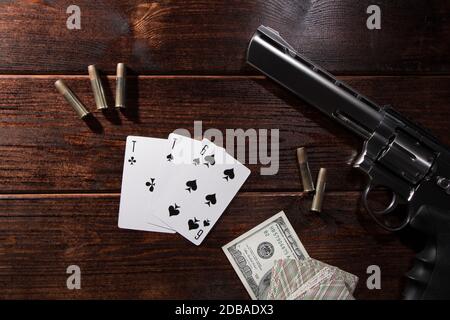 Jouer au poker ou au blackjack pour l'argent. Sur une table en bois se trouvent un pistolet avec des cartouches, des dollars de trésorerie, et une terrasse de cartes de jeu avec un ACE de spa Banque D'Images