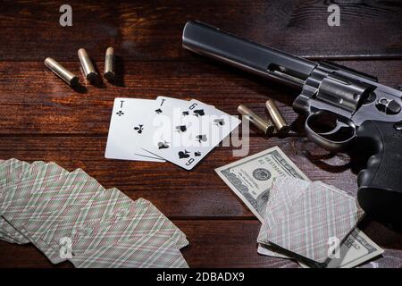 Jouer au poker ou au blackjack pour l'argent. Sur une table en bois se trouvent un pistolet avec des cartouches, des dollars de trésorerie, et une terrasse de cartes de jeu avec un ACE de spa Banque D'Images