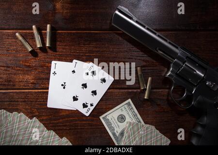 Jouer dans des cartes, poker ou blackjack pour l'argent. Sur une table en bois sont un pistolet avec des cartouches, des dollars de trésorerie, et un jeu de cartes de jeu avec un ACE Banque D'Images